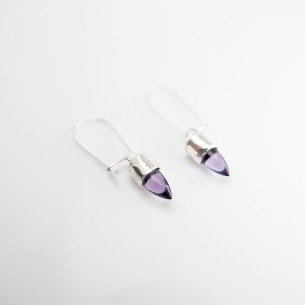 Close up of silver hanging earrings with amethyst in the shape of a bullet.