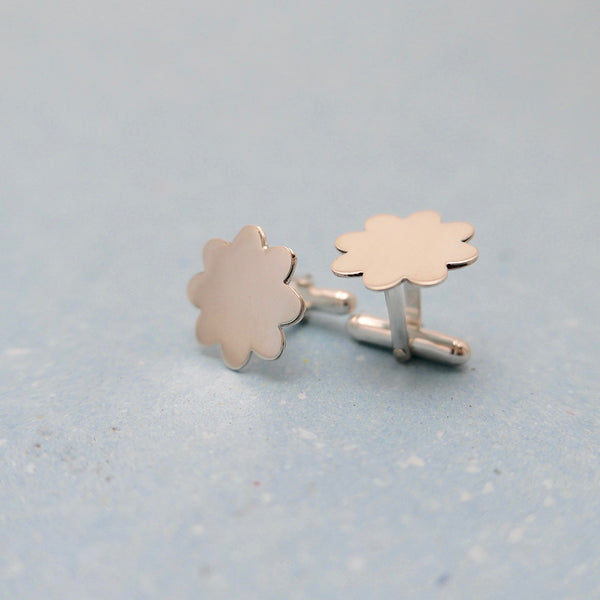 Silver flower cufflinks with on standing and one on its side.