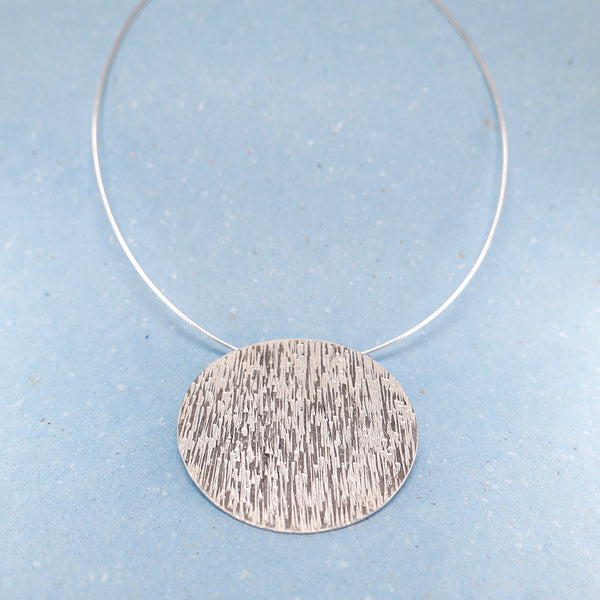 Close up of sterling silver hammered disc necklace on wire chain, showing the Silversmith craftmanship.