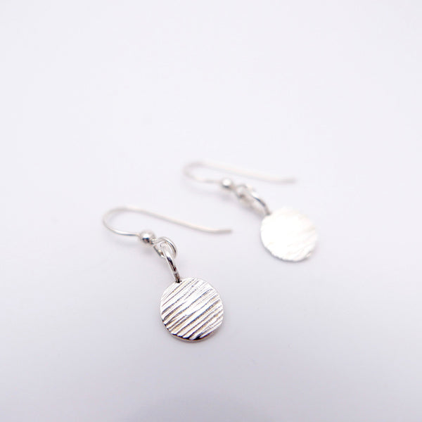 Perspective view of silver dot earrings with handmade hammered lines found on Granville Island Vancouver jewelry.