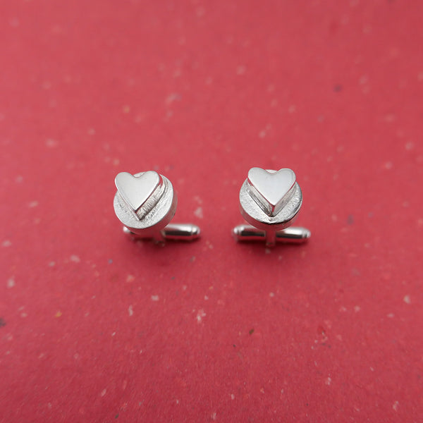 Close up of sterling silver hearts on circle cufflinks on red background.