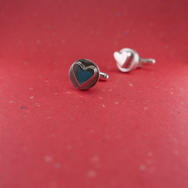 Perspective view of silver heart cufflinks with one close up and the other in the distance.