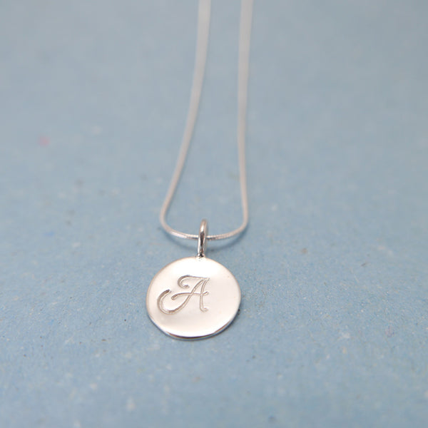 Close up of silver pendant with the letter a stamped on wire chain necklace